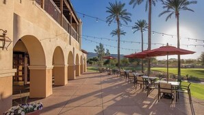 A building with arched walkways and outdoor seating areas with tables and chairs, surrounded by palm trees. - Wyndham 1-Bedroom Studio in a Premier Resort with Full Amenities (Phoenix)