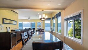 A long dining table with chairs, a chandelier, and large windows with a view of the water. - Private Dock, Kayaks, SUPs, Lakefront Views (Celista)