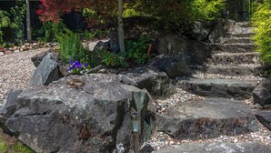 A garden with large rocks, a metal post, and various plants. - Private Dock, Kayaks, SUPs, Lakefront Views (Celista)