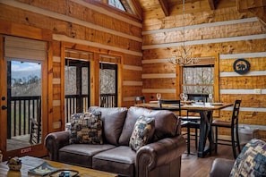 A cozy cabin interior with a leather sofa, dining table, and wooden walls. - Little Bear-NEW RENTAL-TRUSTED HOST! 2BR-Panoramic Views-Hot Tub-Updates (Sevierville)