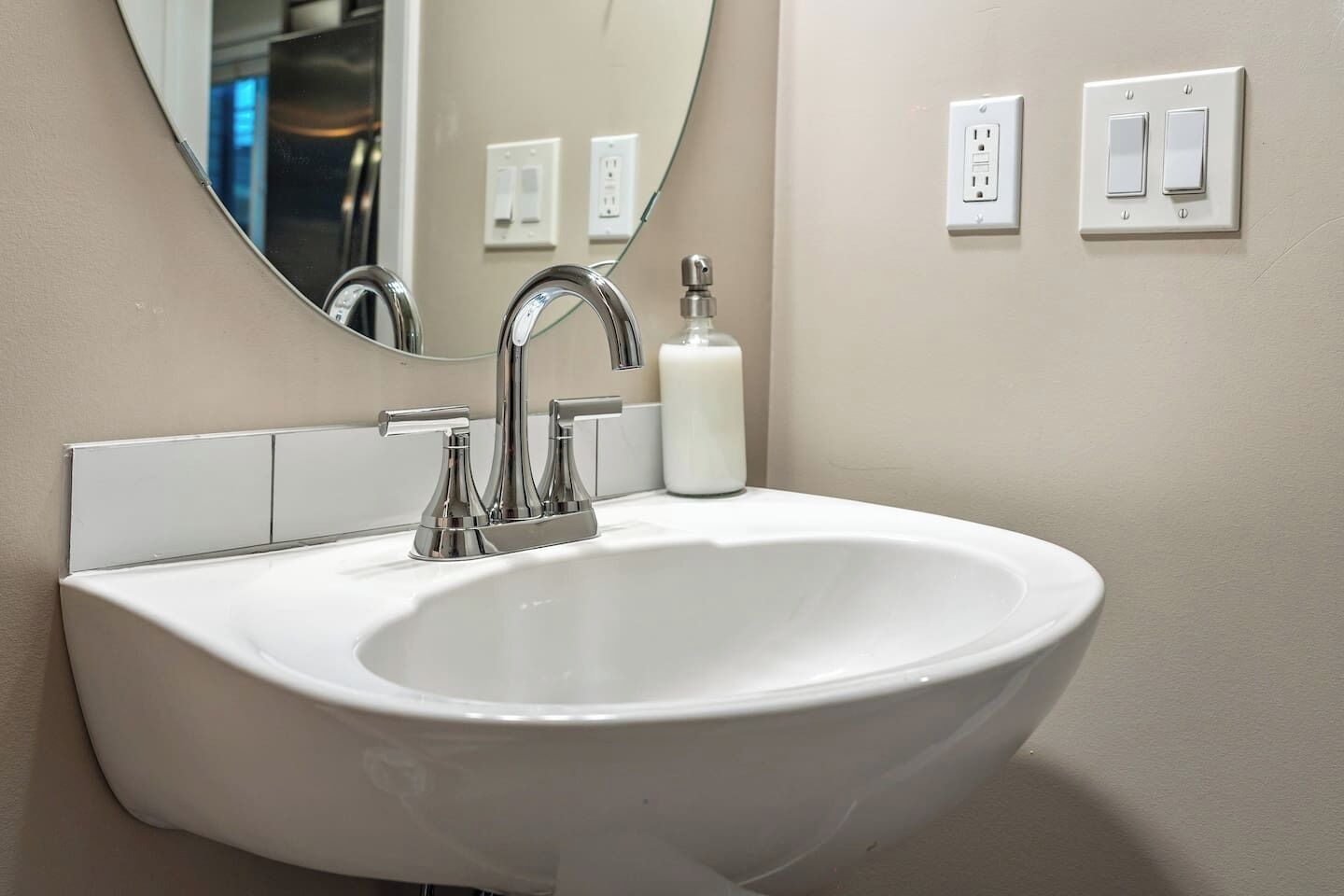 A white bathroom sink with a chrome faucet, a mirror above it, and a wall-mounted light switch.
