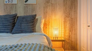 Une chambre avec un mur en bois, un lit avec une literie grise et blanche, et une table de chevet avec une lampe.