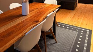Een moderne woonkamer met een houten eettafel, witte stoelen, een zwarte bank en een plafondlamp.