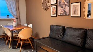 Een moderne woonkamer met een zwarte leren bank, een houten eettafel met stoelen en een raam met gordijnen.