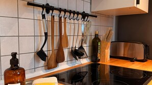 Een moderne keuken met een zwart inductiekookplaatje, een houten aanrechtblad en diverse keukengerei dat aan een rek hangt.