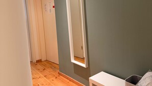 Een gang met houten vloer, een witte bank, een spiegel aan de muur en een hangende tas.