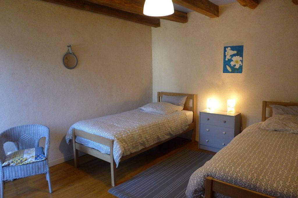 Een slaapkamer met twee enkele bedden, een nachtkastje, een stoel en een lamp aan de muur.