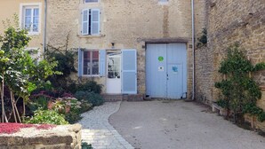 Un bâtiment en pierre avec une allée en gravier et un petit jardin agrémenté de plantes et d’un arbre.