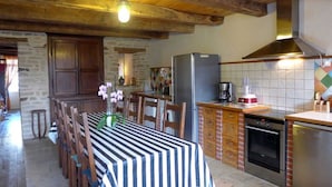 Une cuisine rustique avec un plafond en bois, une table à manger recouverte d’une nappe à rayures et un réfrigérateur.