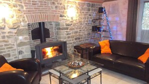 Un salon chaleureux avec un mur en pierre, une cheminée, un canapé en cuir noir et une table basse en verre.