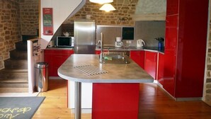 Une cuisine avec des meubles de rangement rouges, un réfrigérateur en acier inoxydable, un four à micro-ondes et un luminaire suspendu.