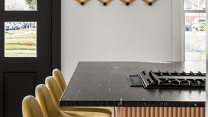 A modern kitchen with a black countertop, yellow chairs, and a unique wooden light fixture. - Assemble Boise (Boise)