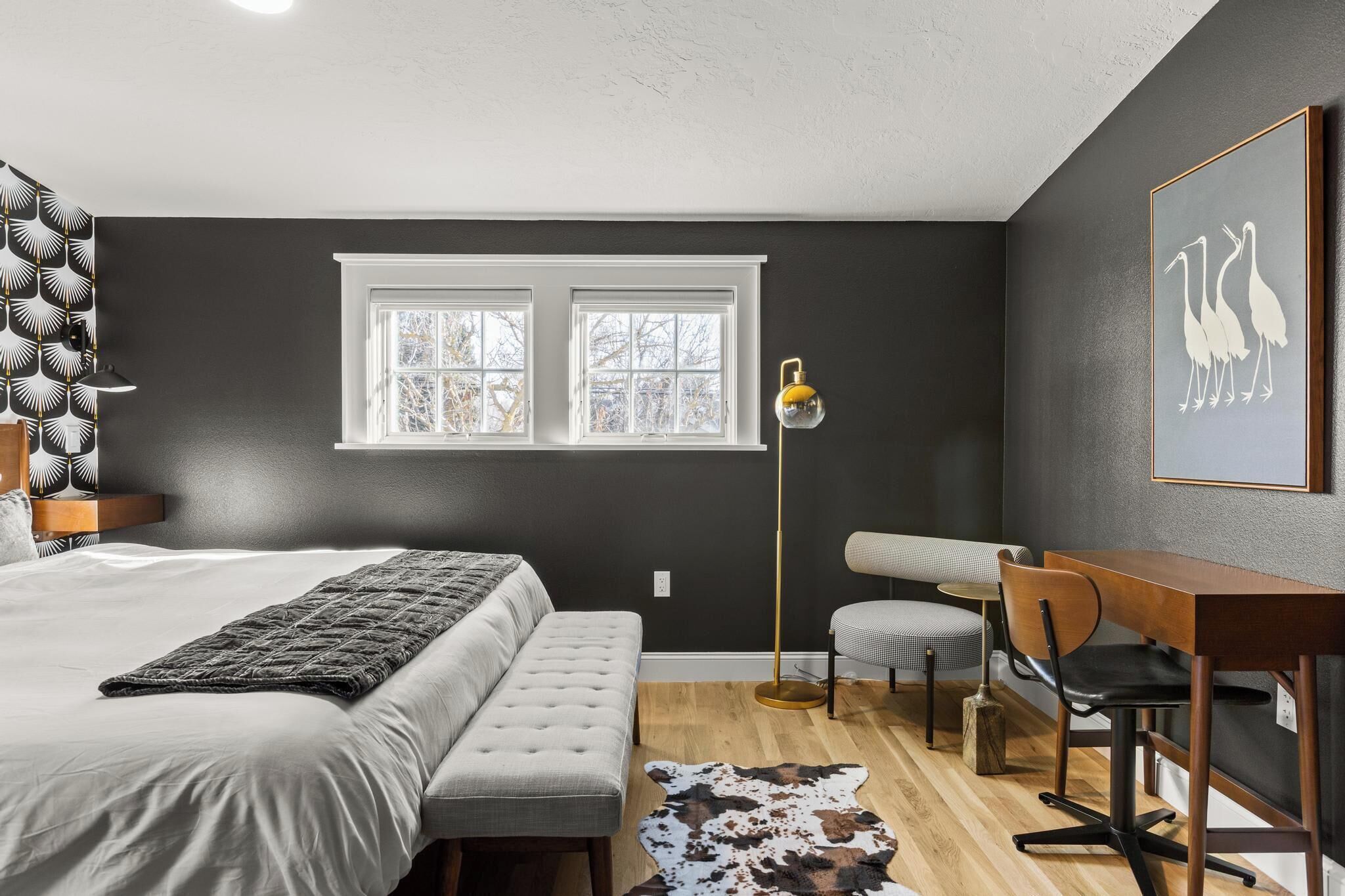 A bedroom with a bed, bench, desk, chair, and a cowhide rug.