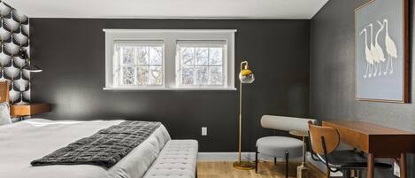 A bedroom with a bed, bench, desk, chair, and a cowhide rug.