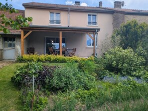 Una casa de dos pisos con un porche cubierto, un jardín con diversas plantas y una antena parabólica en el techo.