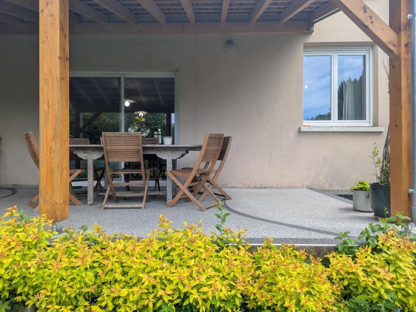 A covered patio with a table and chairs, a window, and a potted plant.