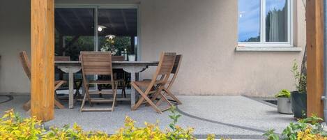 A covered patio with a table and chairs, a window, and a potted plant.