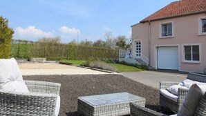 En bostadsfastighet med en asfalterad uppfart, en utomhusplats med möbler av rotting, en tvåvåningsbyggnad med ett rött tegeltak och en välanlagd trädgård.