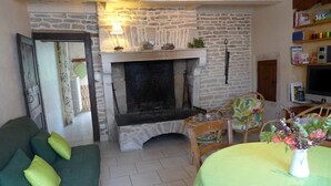 A cozy living room with a stone fireplace, a green sofa, and a table with a vase of flowers. - Gabrielle's House (Giey-sur-Aujon)