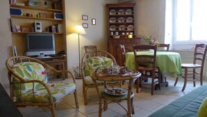A cozy living room with a television, wicker chairs, a dining table with a green tablecloth, and a bookshelf with various items. - Gabrielle's House (Giey-sur-Aujon)