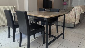 A dining area with a glass-top table, black chairs, a television, and a sofa with a floral cover. - Simone de Beauvoir Guesthouse (Châteauvillain)