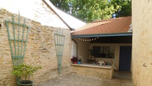 A courtyard with a stone wall, a gravel floor, a potted plant, and a small seating area with a table and chairs. - Simone de Beauvoir Guesthouse (Châteauvillain)