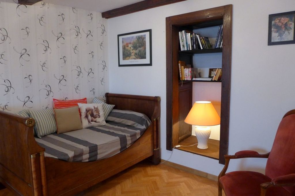 A cozy room with a wooden bed, a red chair, a bookshelf, and a lamp.