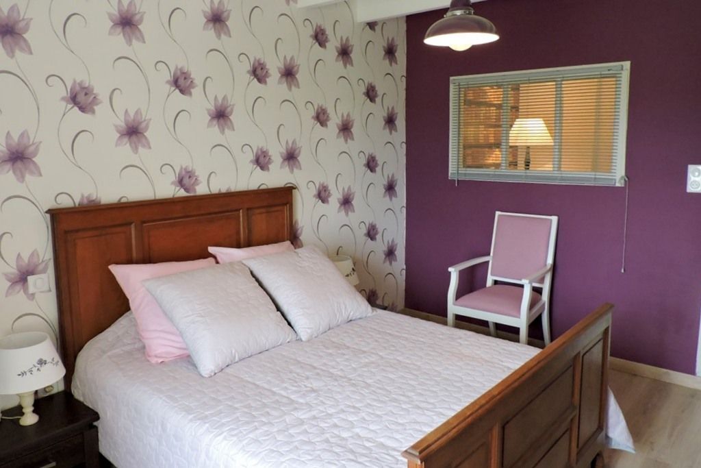 Une chambre à coucher avec un lit en bois, une chaise, une table de chevet et une fenêtre avec des stores.