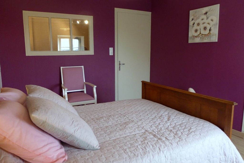 Een slaapkamer met een bed, kussens, een stoel, een deur en een spiegel aan de muur.