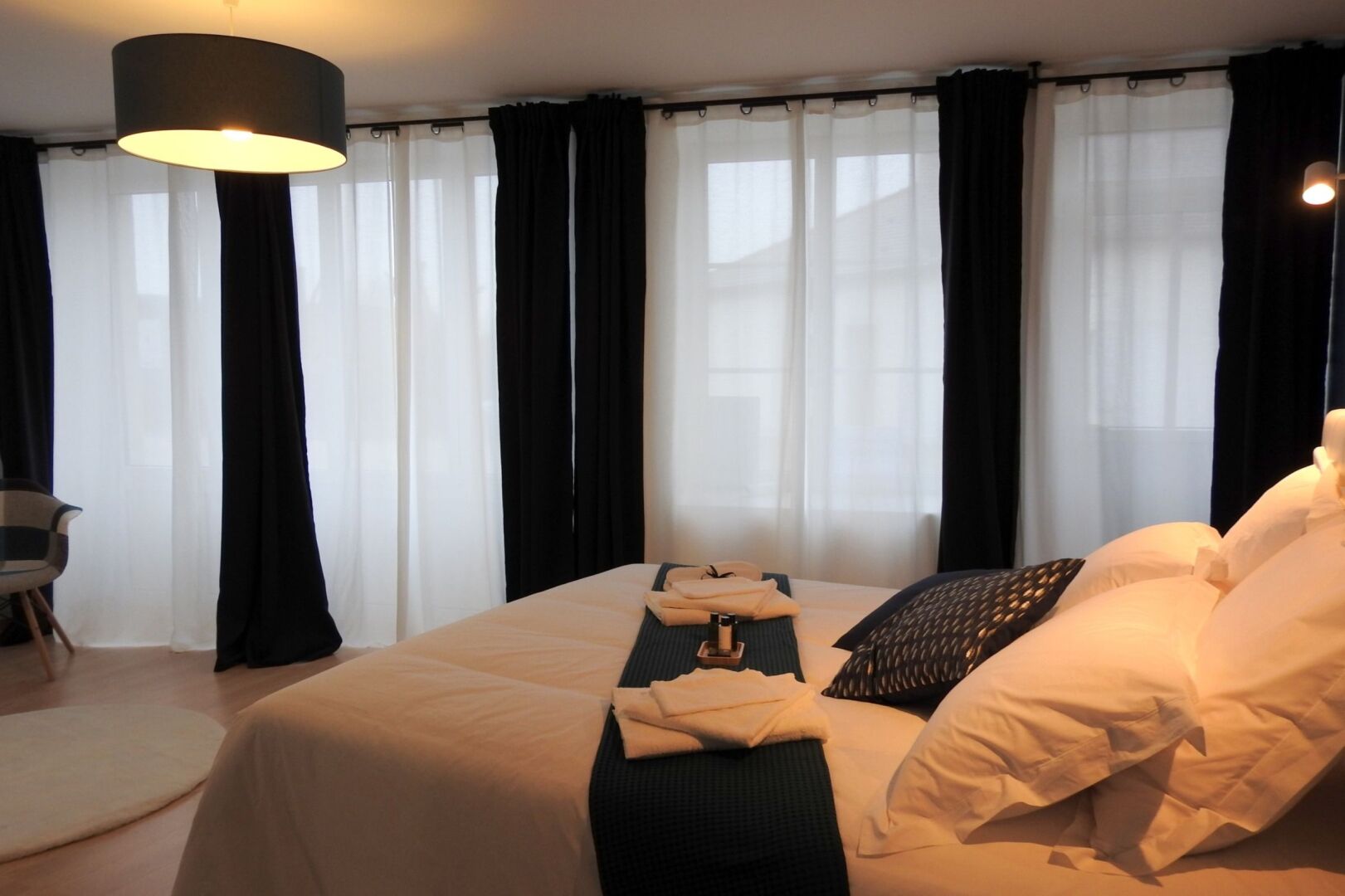 Ein Hotelzimmer mit einem großen Bett, schwarz-weißen Vorhängen, einem runden Tisch mit einer Lampe und einem Sessel.