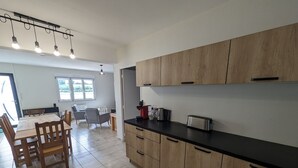 Cuina moderna amb armaris de fusta, taulell negre i zona de dinar amb taula i cadires.