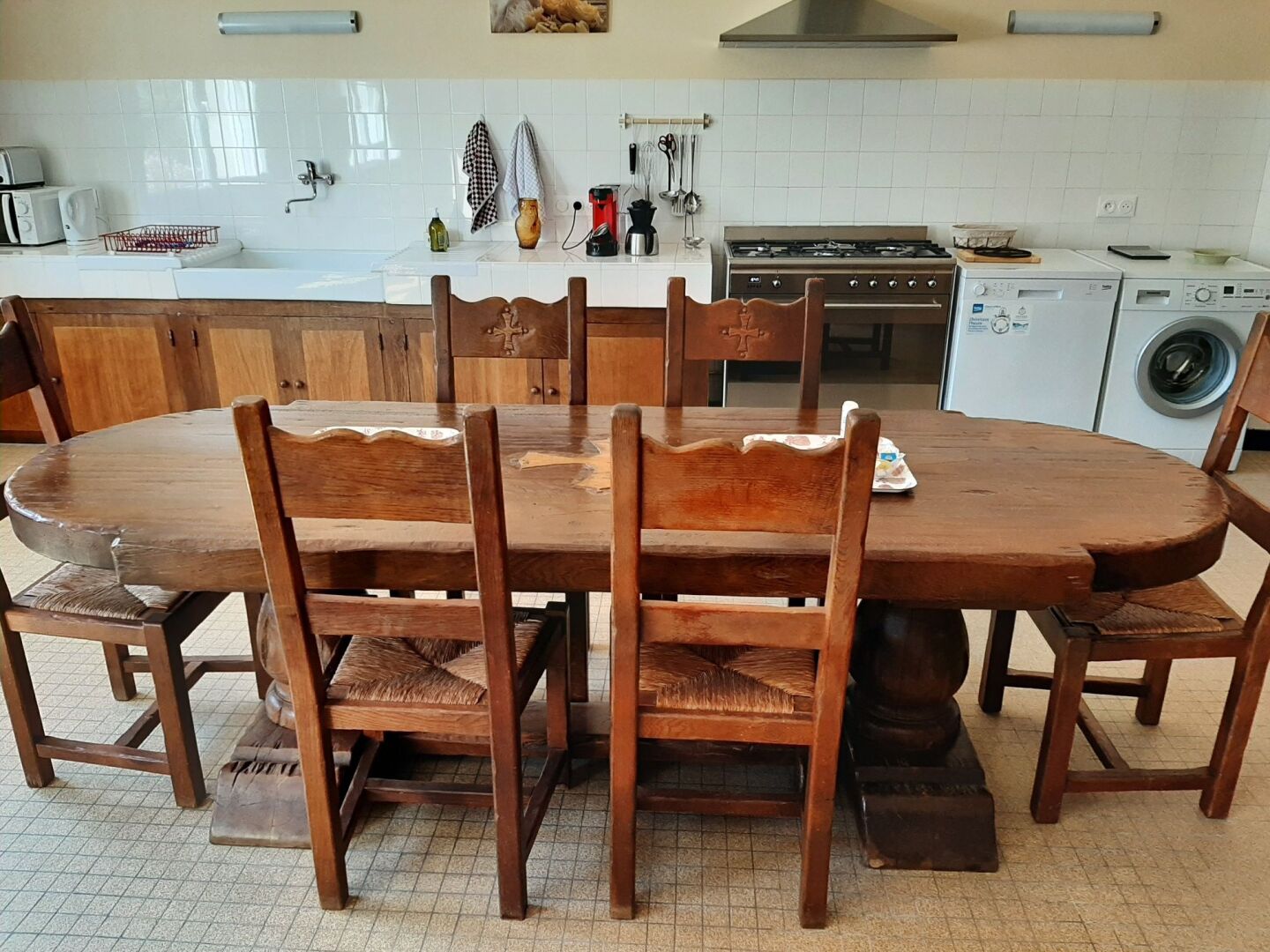 Eine Küche mit einem Holzespeisetisch, Stühlen, einem Herd, einer Waschmaschine und einer gefliesten Spritzschutzwand.