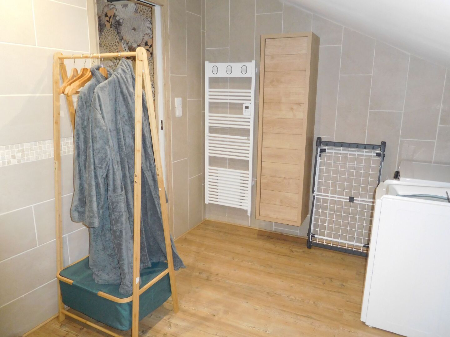 A small, cozy bathroom with a wooden floor, a towel rack with a towel, a white radiator, and a wooden cabinet.