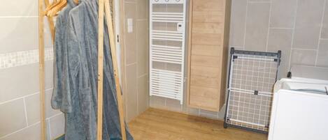 A small, cozy bathroom with a wooden floor, a towel rack with a towel, a white radiator, and a wooden cabinet.