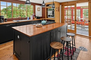 A modern kitchen with a central island, bar stools, and a view of the outdoors. - 17-Acre Farmhouse Retreat | Mountain Views, Trails (Lovell)