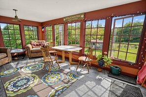 A sunlit room with a table and chairs, large windows, and a view of greenery. - 17-Acre Farmhouse Retreat | Mountain Views, Trails (Lovell)