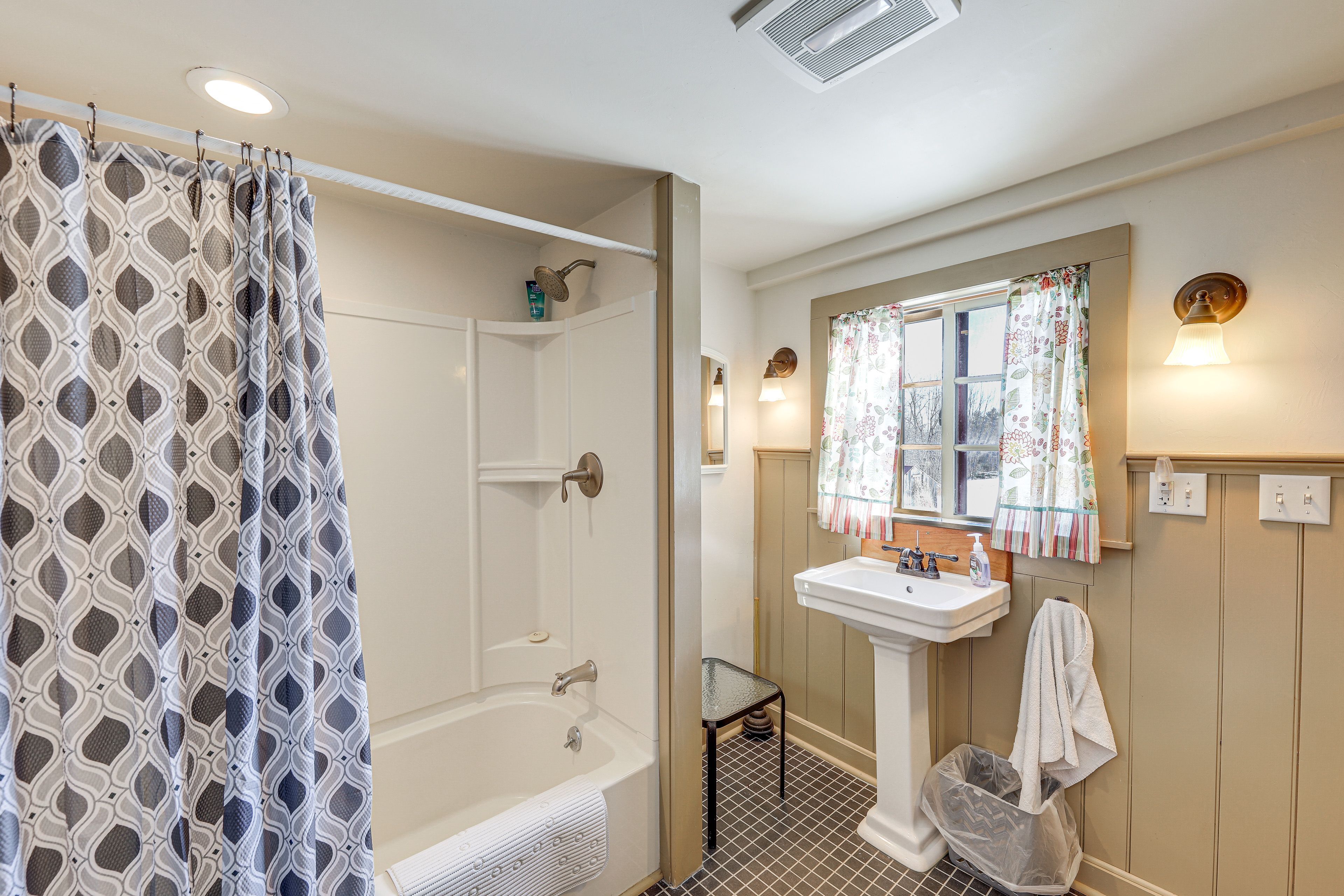 A bathroom with a shower, a sink, and a window with a curtain.