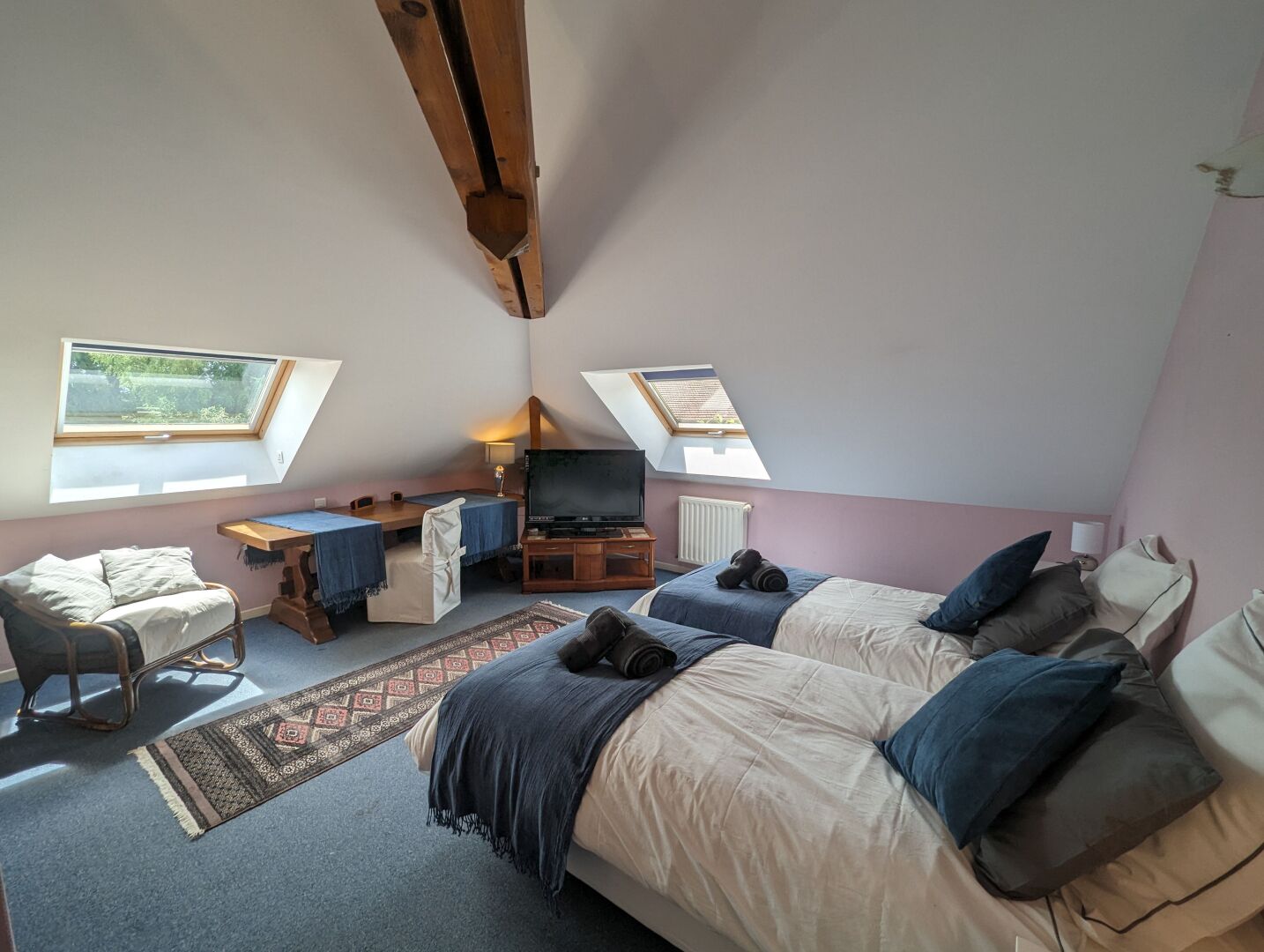 A cozy attic bedroom with two beds, a desk, a TV, and skylights.