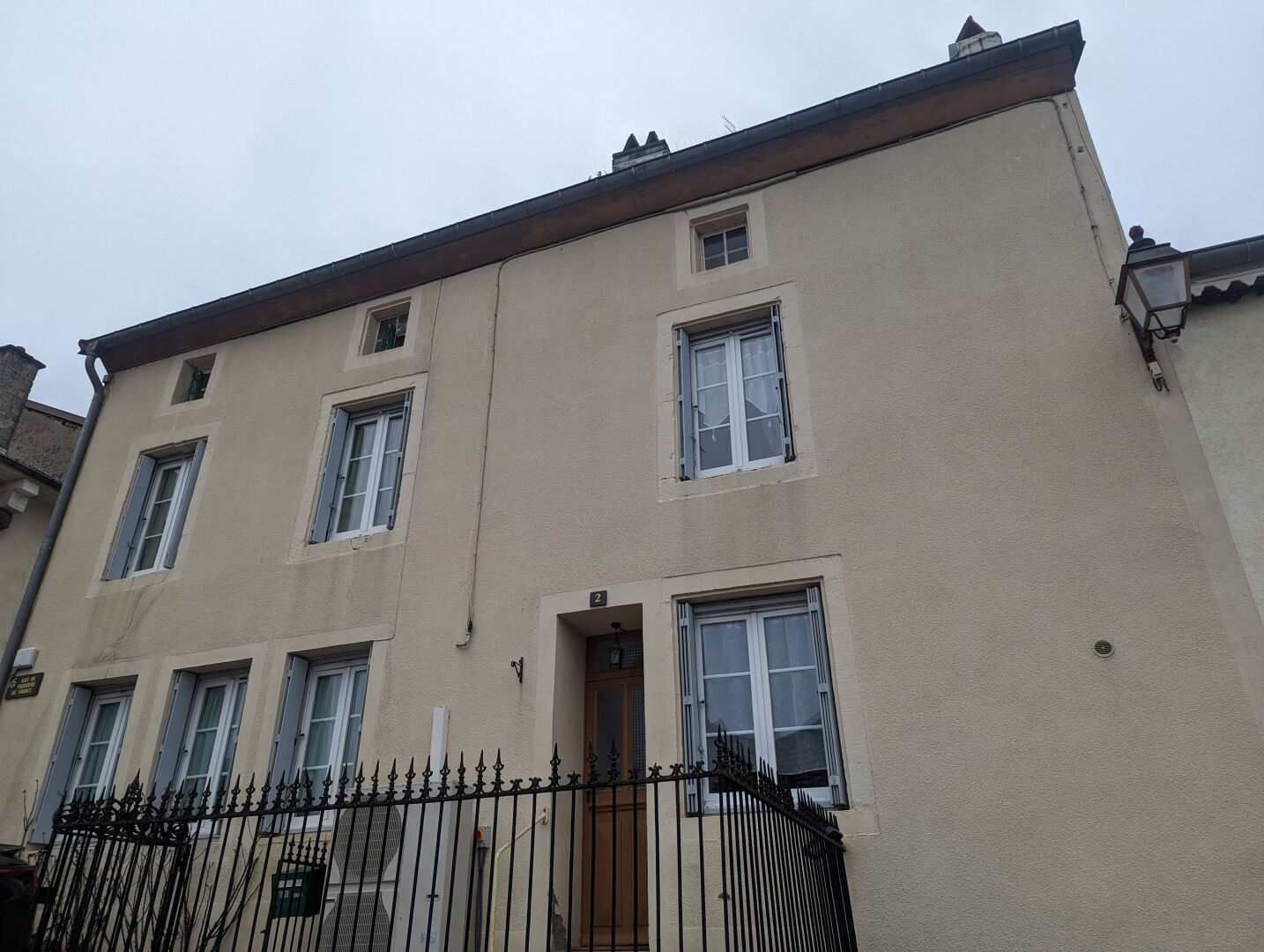 Ein mehrstöckiges Gebäude mit hellbeiger Fassade, zahlreichen Fenstern und einem schwarzen Metallzaun im Vordergrund.