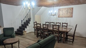 A dining area with a wooden table and chairs, a green sofa, and a staircase with a chandelier. - Stopover at Côna - Bourmont (Bourmont)