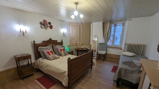 A bedroom with a wooden bed, a nightstand, a chair, a dresser, a radiator, and a window with curtains. - Stopover at Côna - Bourmont (Bourmont)