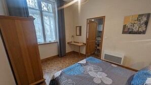 Un dormitorio con cama, armario, ventana y un espejo, además de un cuadro en la pared.