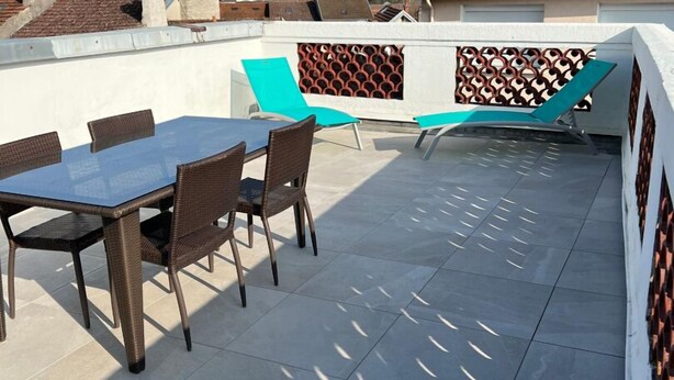 Una terraza en la azotea con una mesa y sillas, un muro con diseño y vistas del barrio circundante.