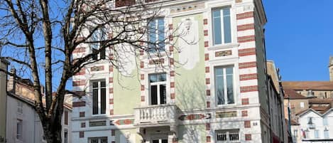 Un edificio de varios pisos con una fachada simétrica, amplias ventanas y una entrada central con un balcón decorativo.