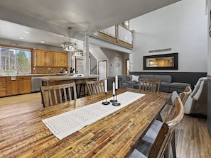 A spacious living room with a large wooden dining table, a grey sofa, and a staircase leading to an upper level.