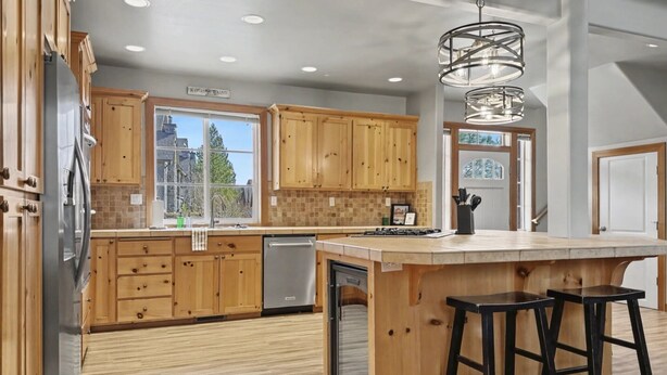 A modern kitchen with wooden cabinets, a central island with stools, and a view of the outside. - Roslyn Pines: Hot Tub, Spacious Deck, Dogs Welcome, Family Friendly! (Ronald)