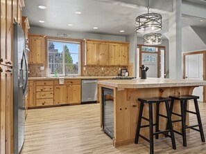 A modern kitchen with wooden cabinets, a central island with stools, and a view of the outside.