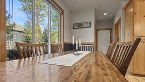 A long wooden dining table with chairs, a welcome sign, and a view of trees and buildings outside. - Roslyn Pines: Hot Tub, Spacious Deck, Dogs Welcome, Family Friendly! (Ronald)