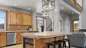 A spacious kitchen with wooden cabinets, a central island with stools, and a modern pendant light. - Roslyn Pines: Hot Tub, Spacious Deck, Dogs Welcome, Family Friendly! (Ronald)