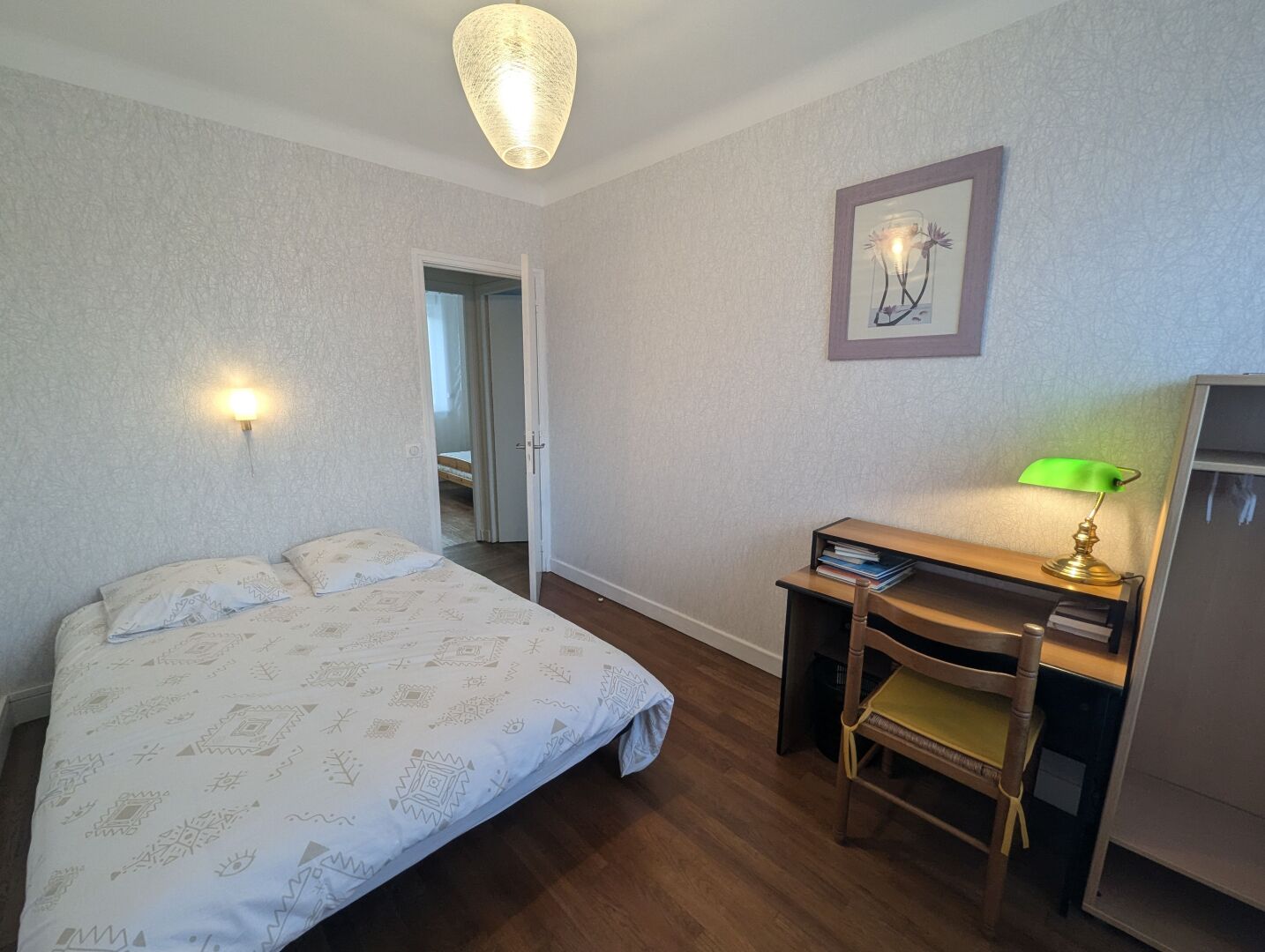 A bedroom with a bed, a desk with a chair, a lamp, and a framed picture on the wall.